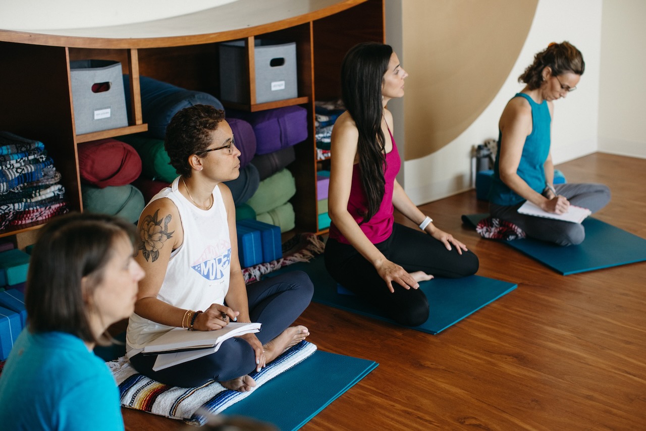 Four women sit in yoga teacher training, listening